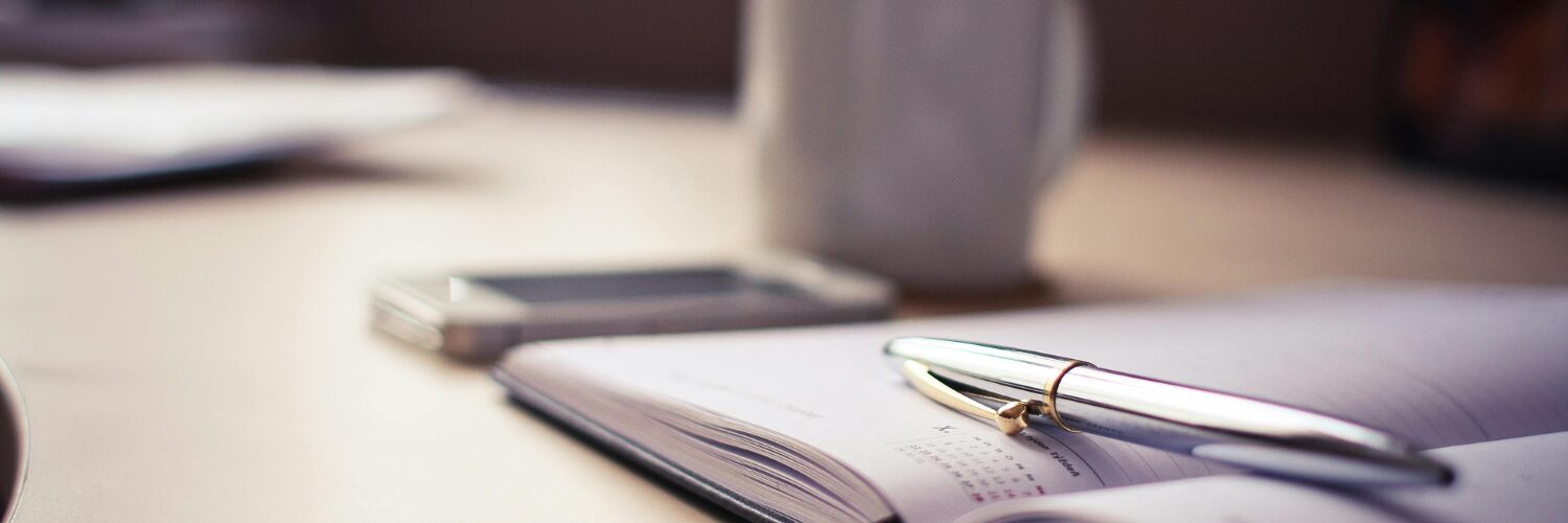Open planner with pen, smartphone, and coffee cup on a desk, representing iWS Australia’s payroll services and rostering management solutions.