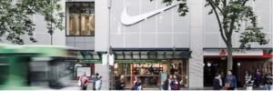 Street view of a Nike retail store with a large white Nike swoosh logo above the entrance and shoppers walking by in an urban shopping area, representing iWS Australia Retailers
