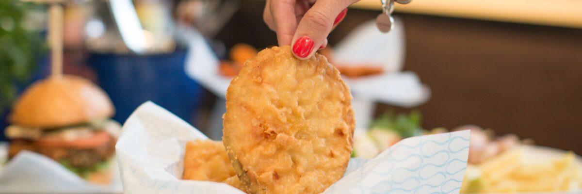 hunky-dory-food A hand lifting a golden, crispy battered slice from a bowl lined with branded paper at Hunky Dory Fish & Chips — a popular iWS Australia franchise known for fresh, high-quality seafood.